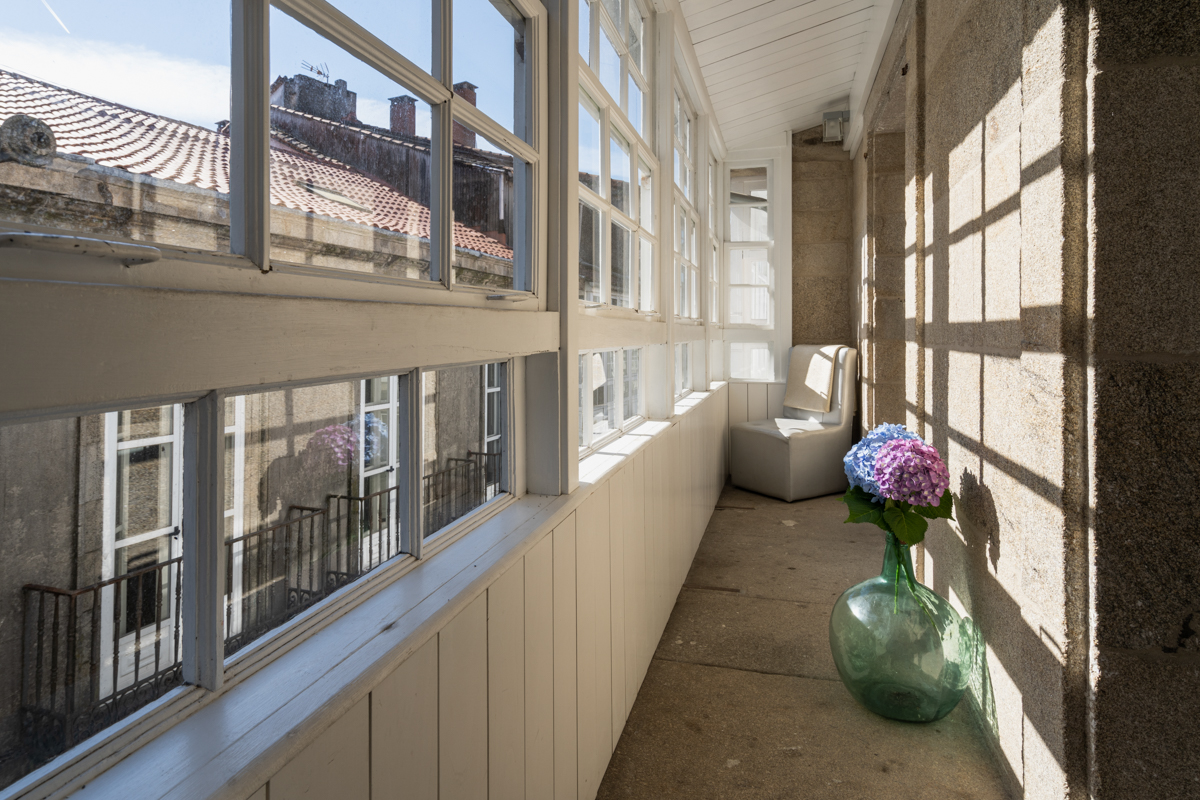 Fotografía de terraza cubierta con vistas a la calle, una silla y un jarrón decorativo en el suelo.