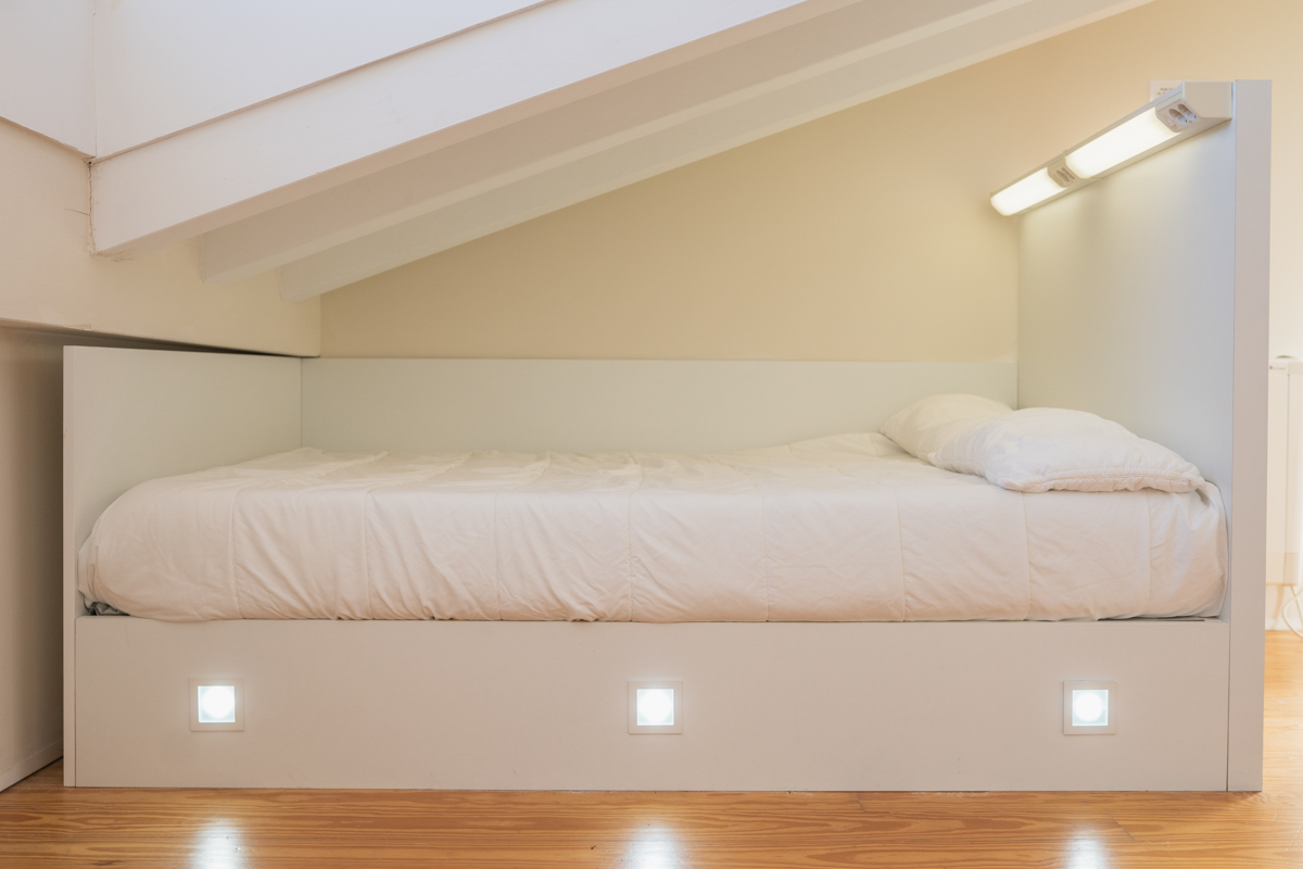 Fotografía de una cama individual con iluminación personalizada en el cabecero y en la base de la cama.